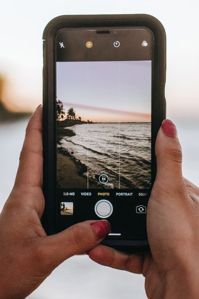 A picture of a beach as the sun is setting through the screen of a smartphone.